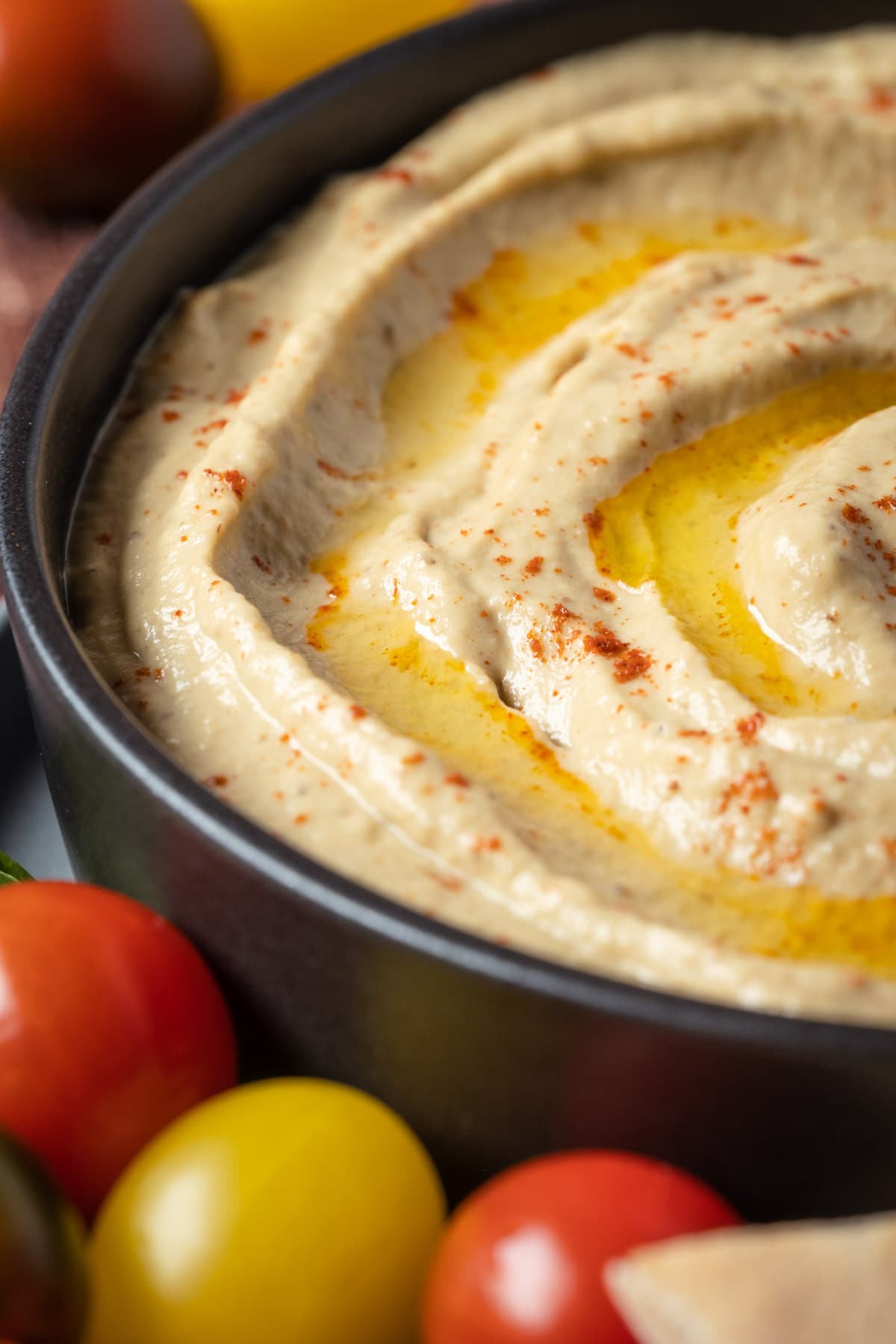 Baba ganoush in a bowl topped with smoked paprika and olive oil, with cherry tomatoes and pita breads on the side.