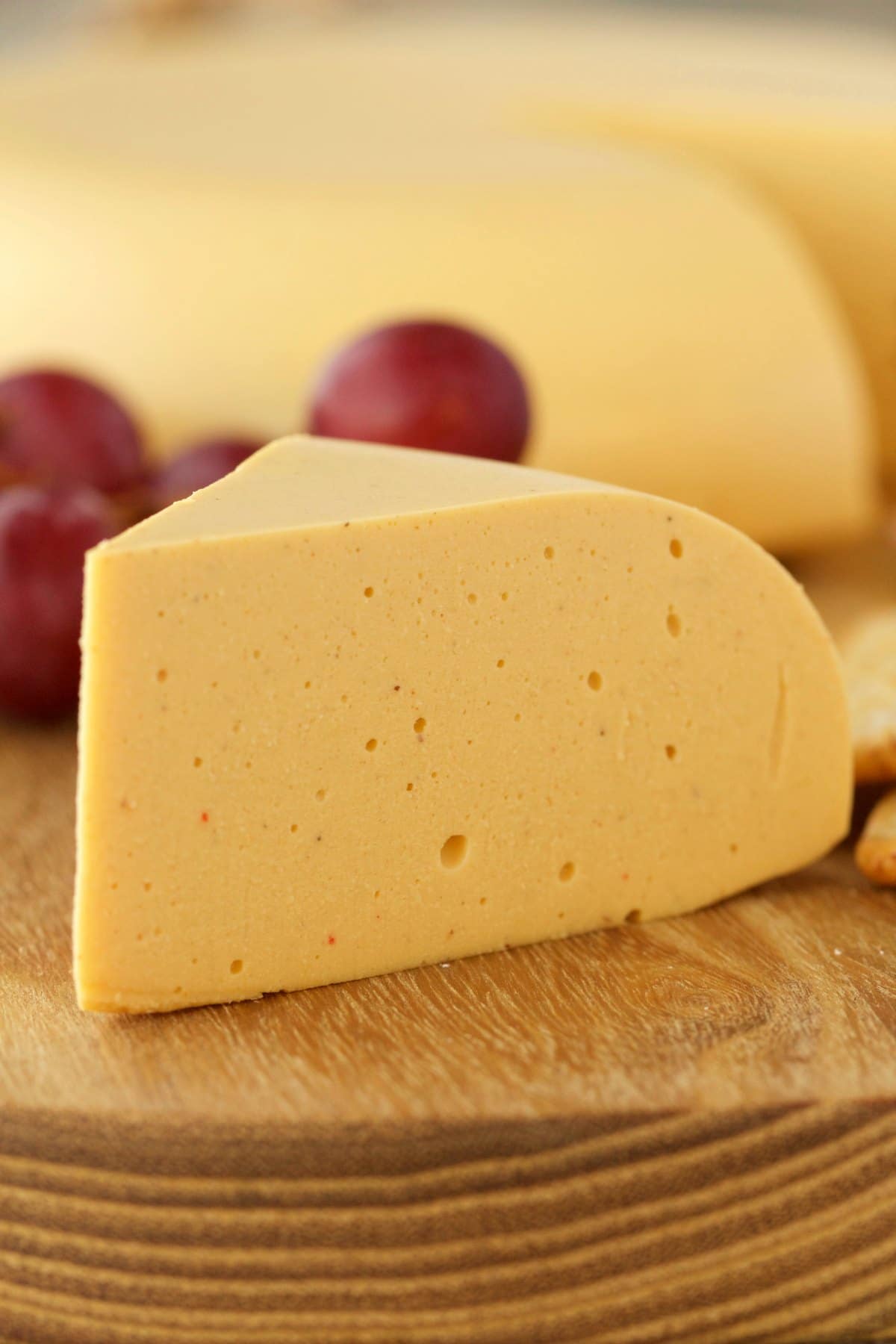 Large wedge of vegan cheese on a cheese board with grapes and crackers. 