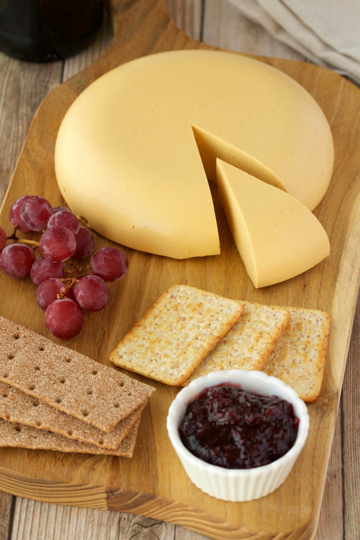 Wheel of vegan cashew cheese on a cheeseboard with crackers, grapes and jam.