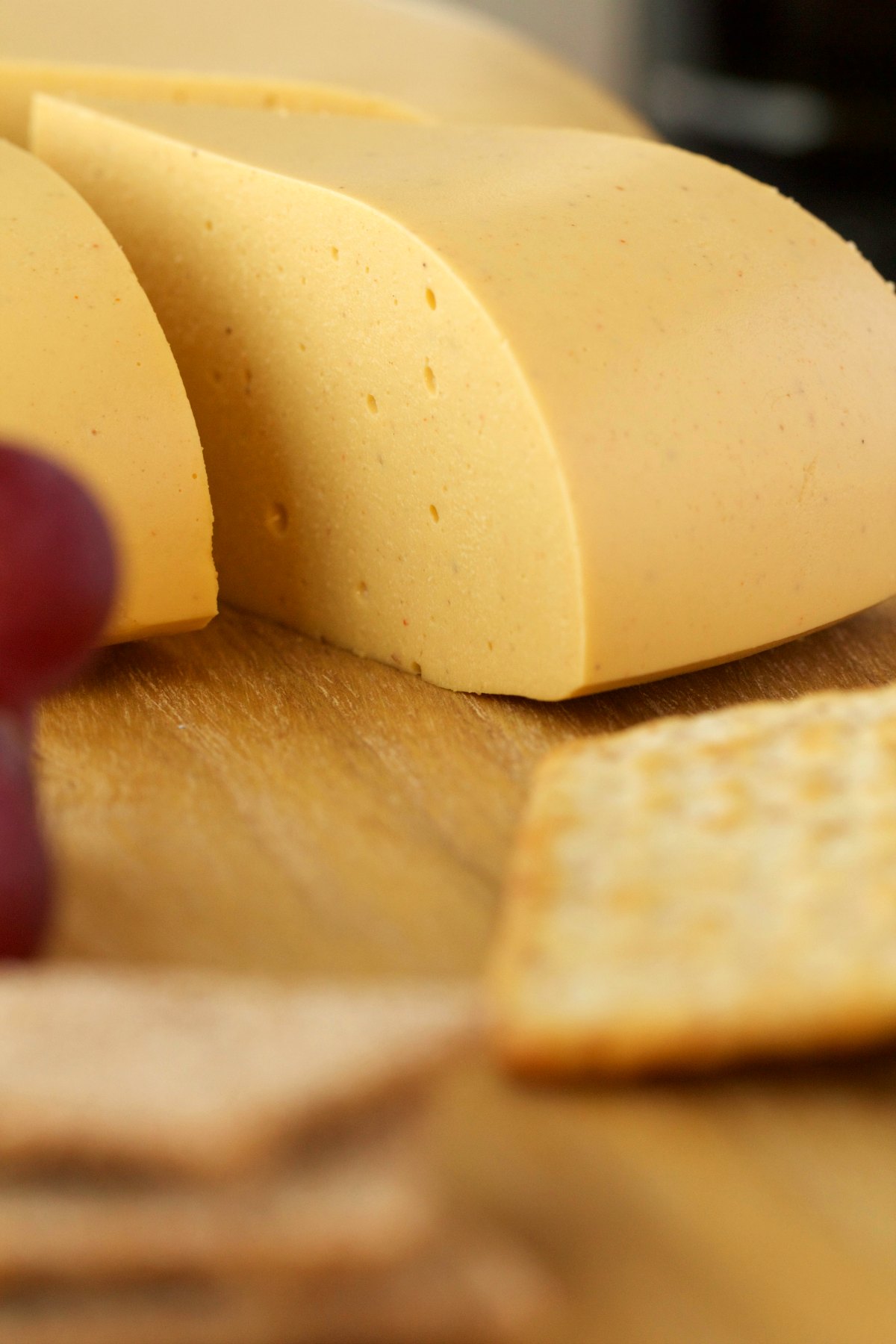 Sliced wheel of cashew cheese on a cheese board with crackers and grapes. 