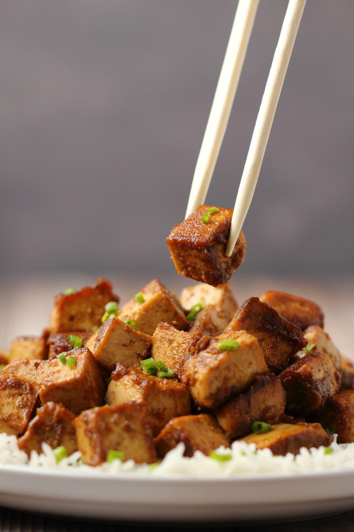Marinated tofu topped with chopped chives on a bed of rice with chopsticks. 