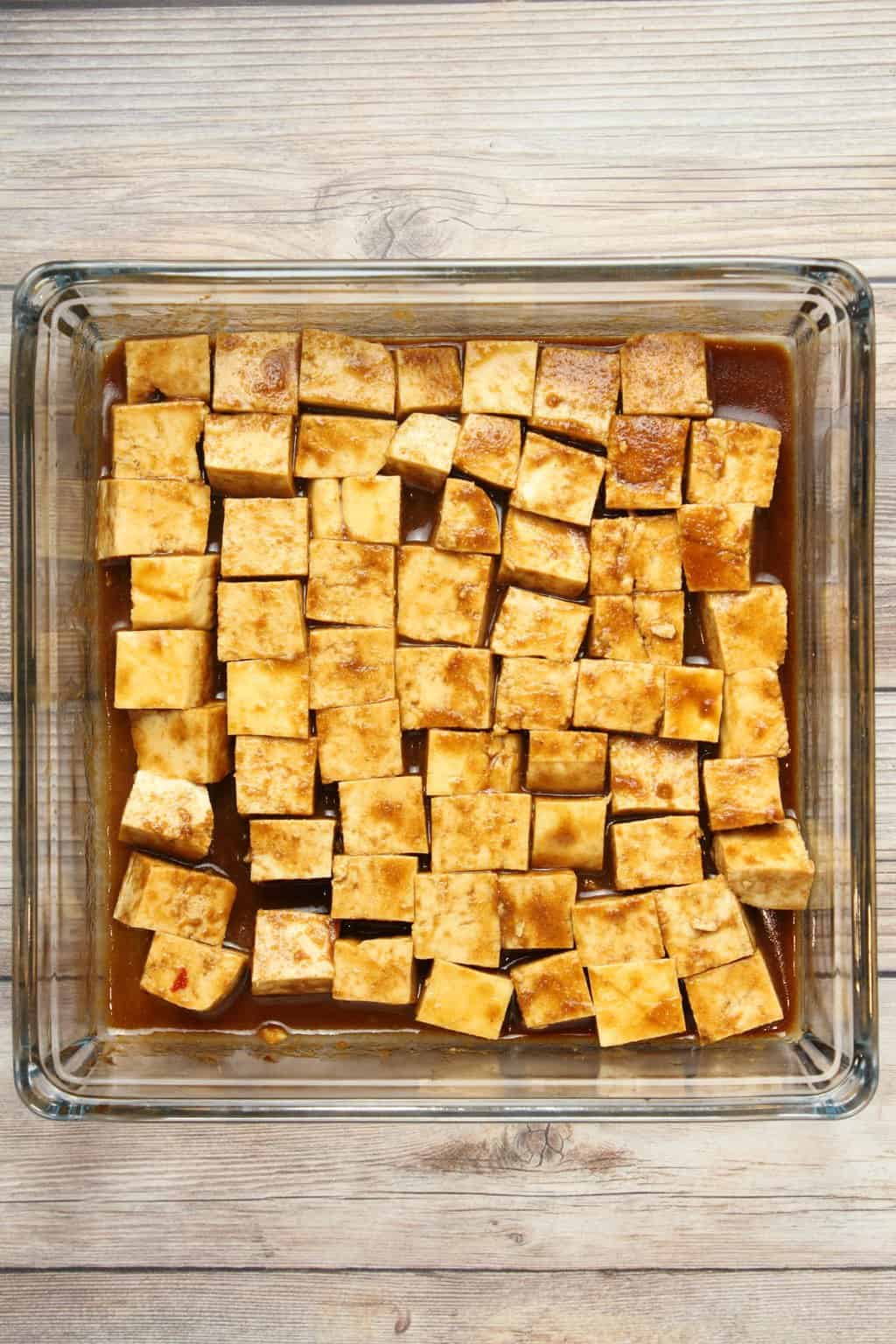 Cubes of tofu marinading in a tofu marinade sauce in a glass dish. 
