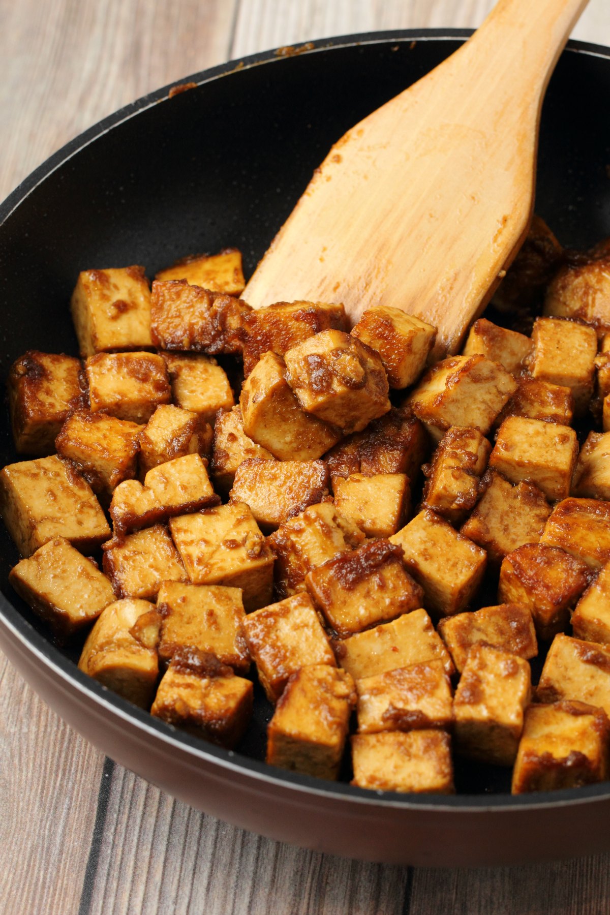 Marinated tofu frying in a pan with a wooden spatula. 