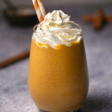 Pumpkin smoothie topped with whipped cream in a glass with a straw.