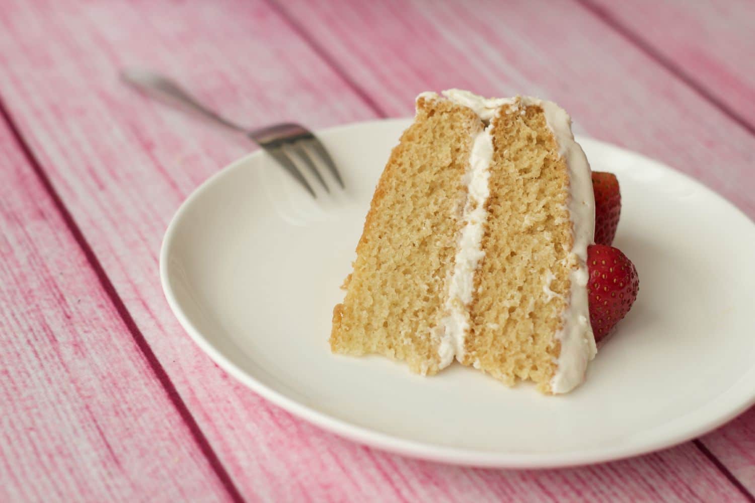 A slice of vegan vanilla cake on a white plate with a cake fork. 