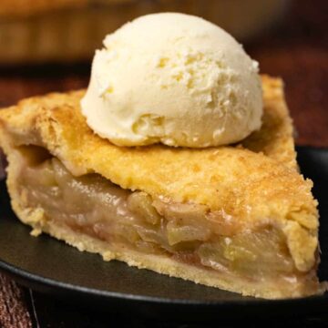 Slice of vegan apple pie topped with ice cream on a black plate.