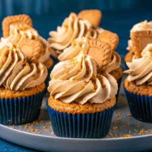Vegan biscoff cupcakes topped with frosting and biscoff cookies on a gray plate.