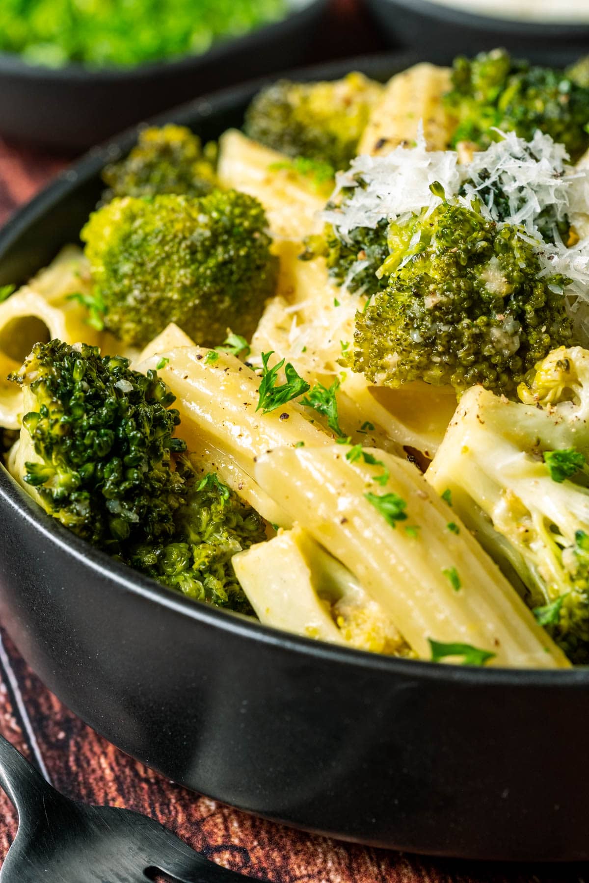 Vegan broccoli pasta topped with vegan parmesan in a black bowl.