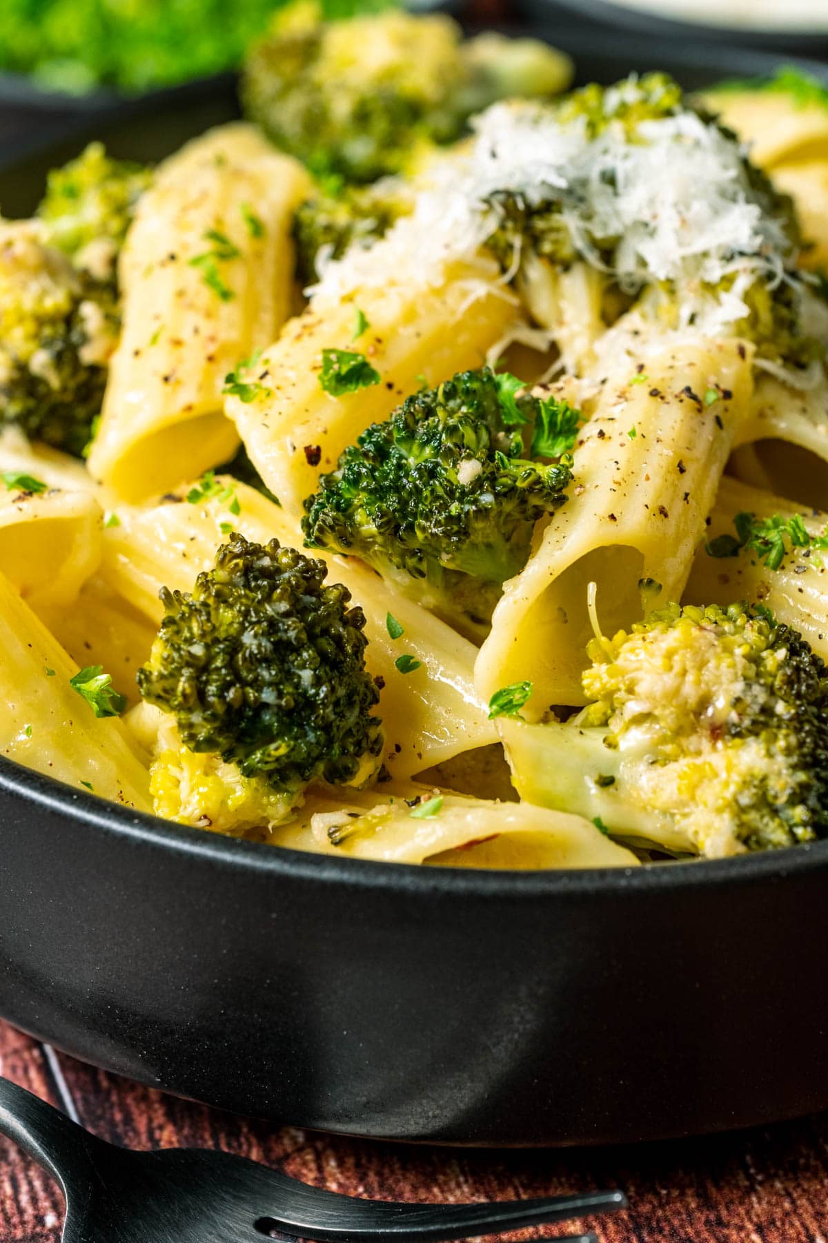 Vegan broccoli pasta topped with vegan parmesan in a black bowl.