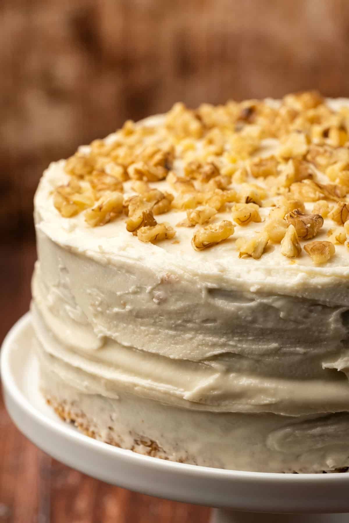 Vegan carrot cake topped with walnuts on a white cake stand.