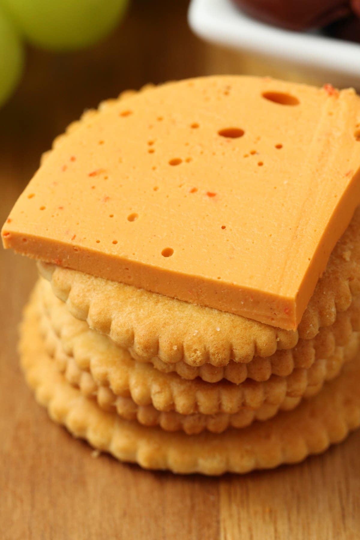 Sliced vegan cheddar cheese on top of a stack of crackers. 