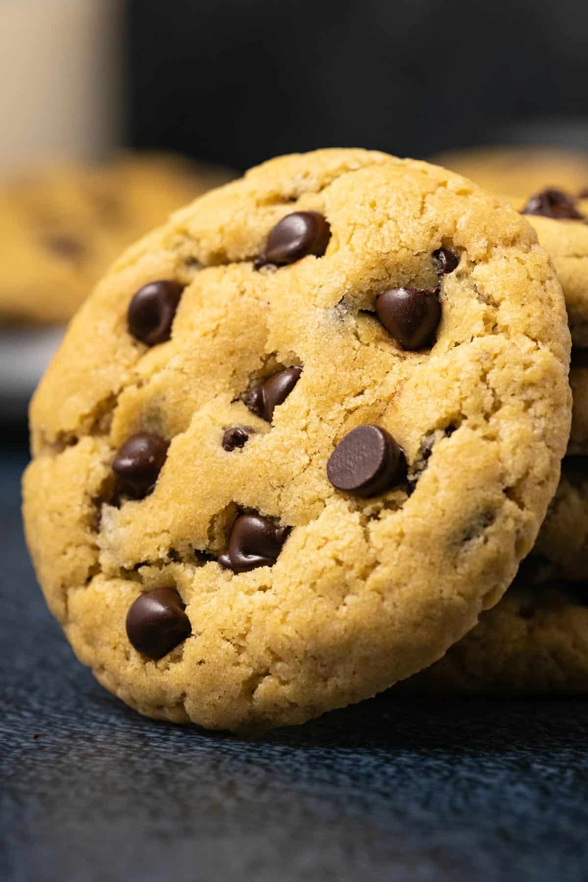 A chocolate chip cookie leaning against a stack of cookies. 