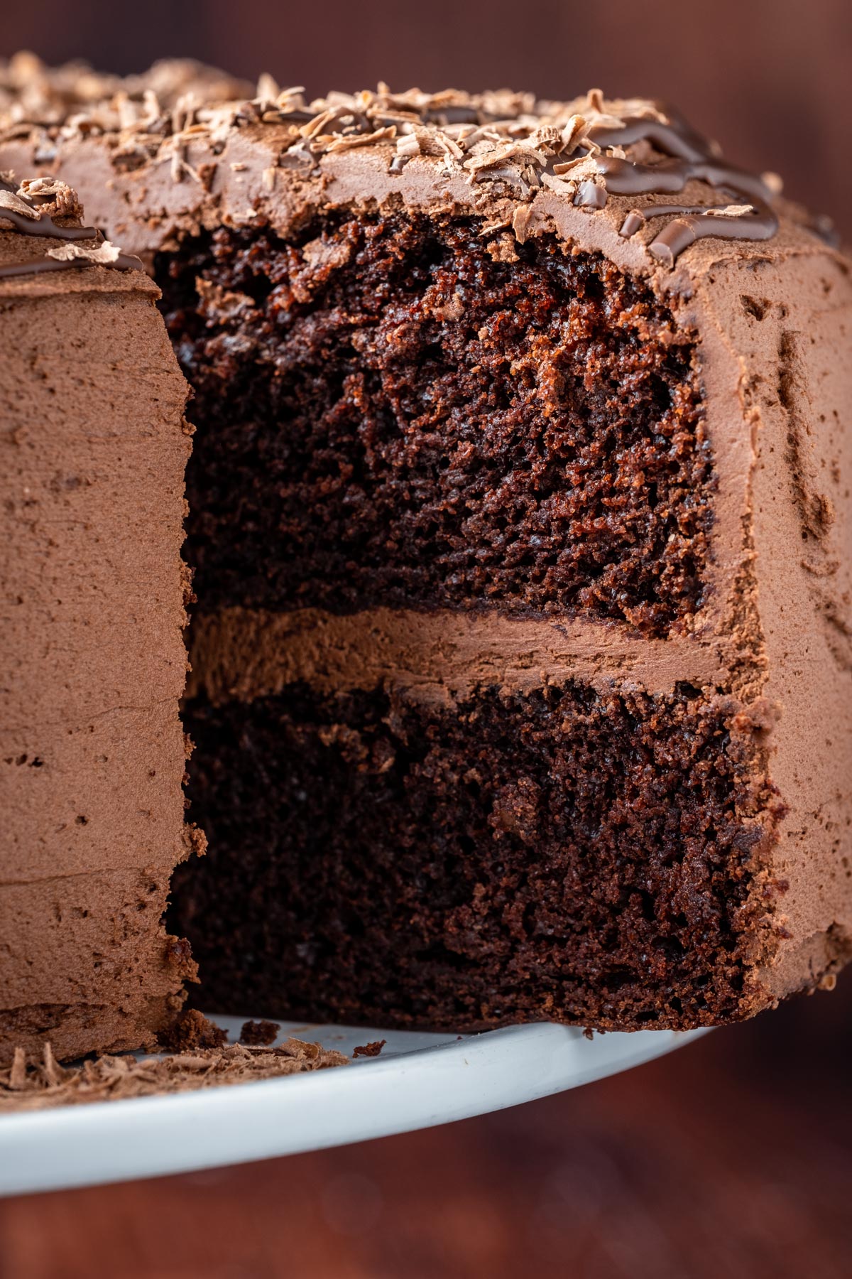 Sliced vegan chocolate fudge cake on a white cake stand.