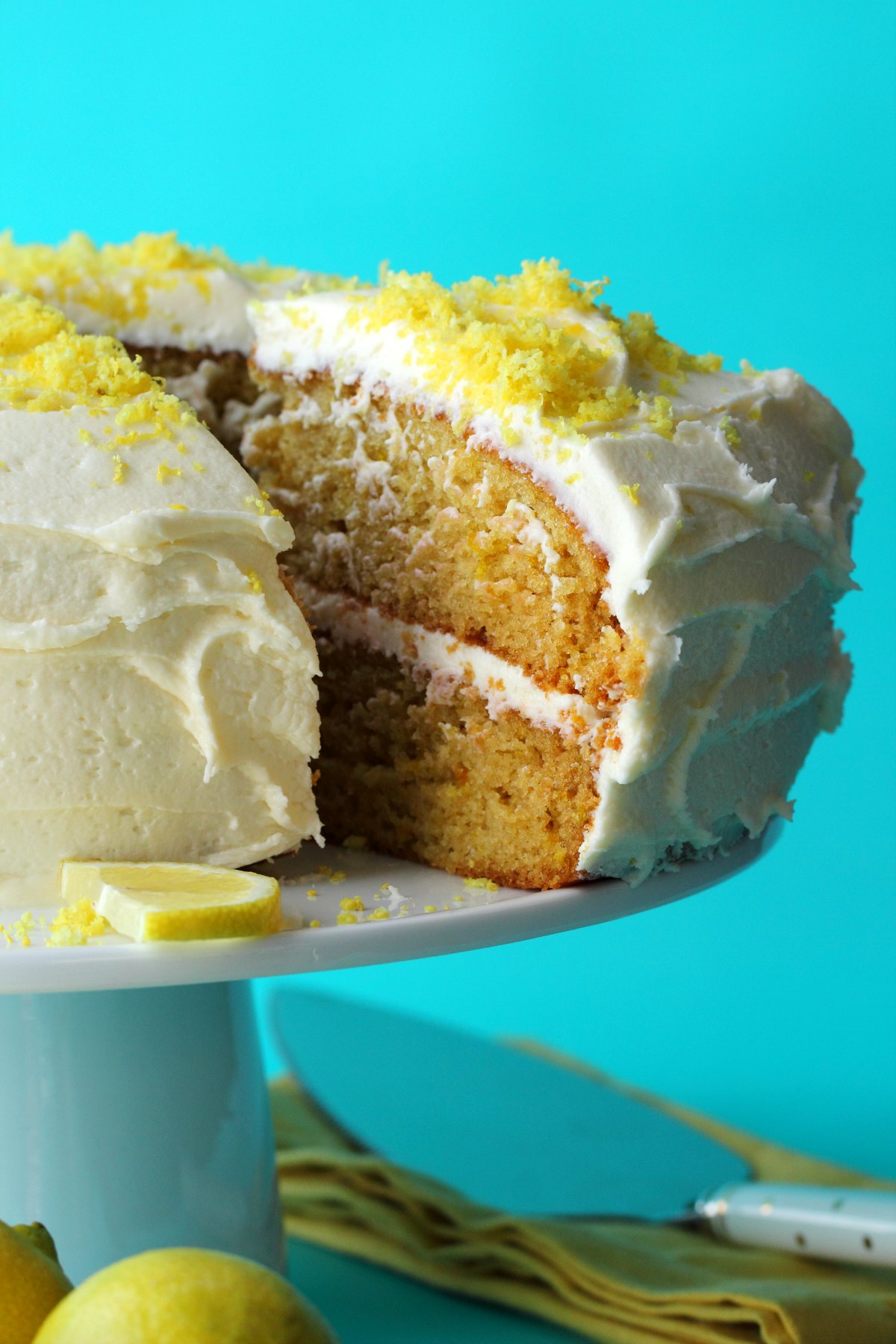 Lemon cake topped with lemon zest on a white cake stand. 