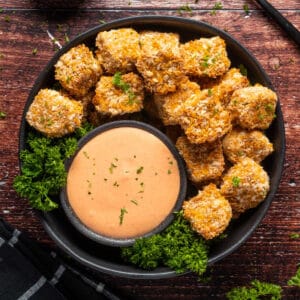 Vegan chicken nuggets stacked up on a plate with fresh parsley and a bowl of yum yum sauce.