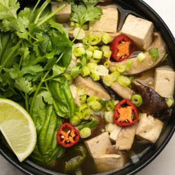 Vegan pho in a black bowl with fresh cilantro and lime.