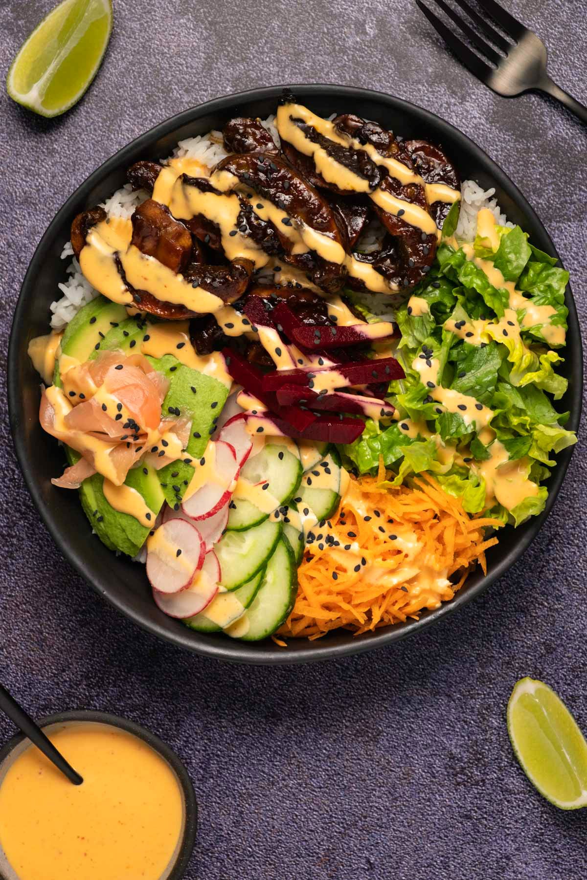 Black bowl filled with rice, salad and veggies and a drizzled dressing. 