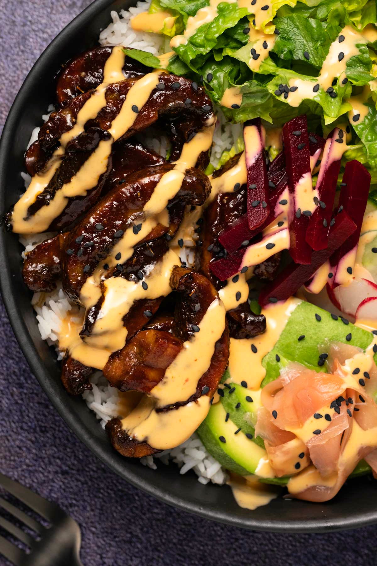Close up of a black bowl filled with rice and veggies and a drizzled dressing. 
