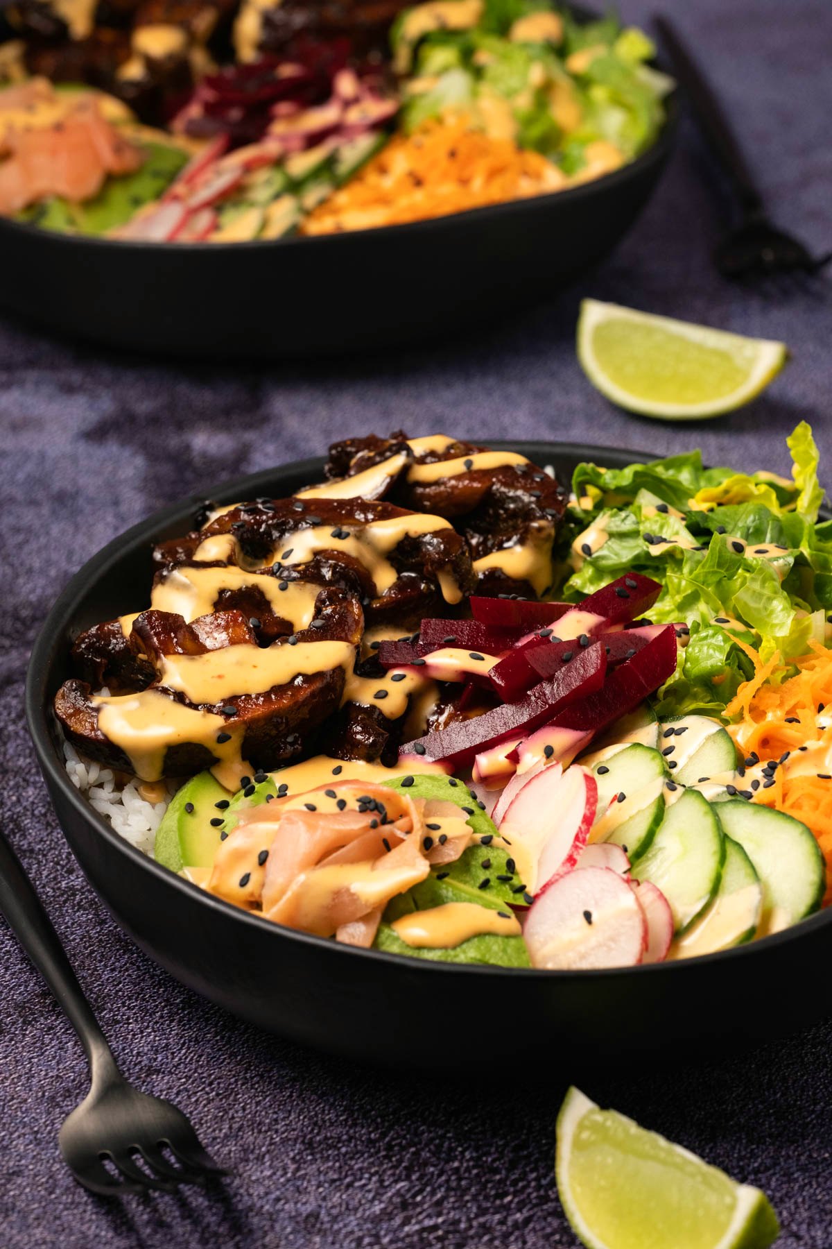 Black bowl with salad and rice and mushrooms, drizzled with a creamy dressing. 
