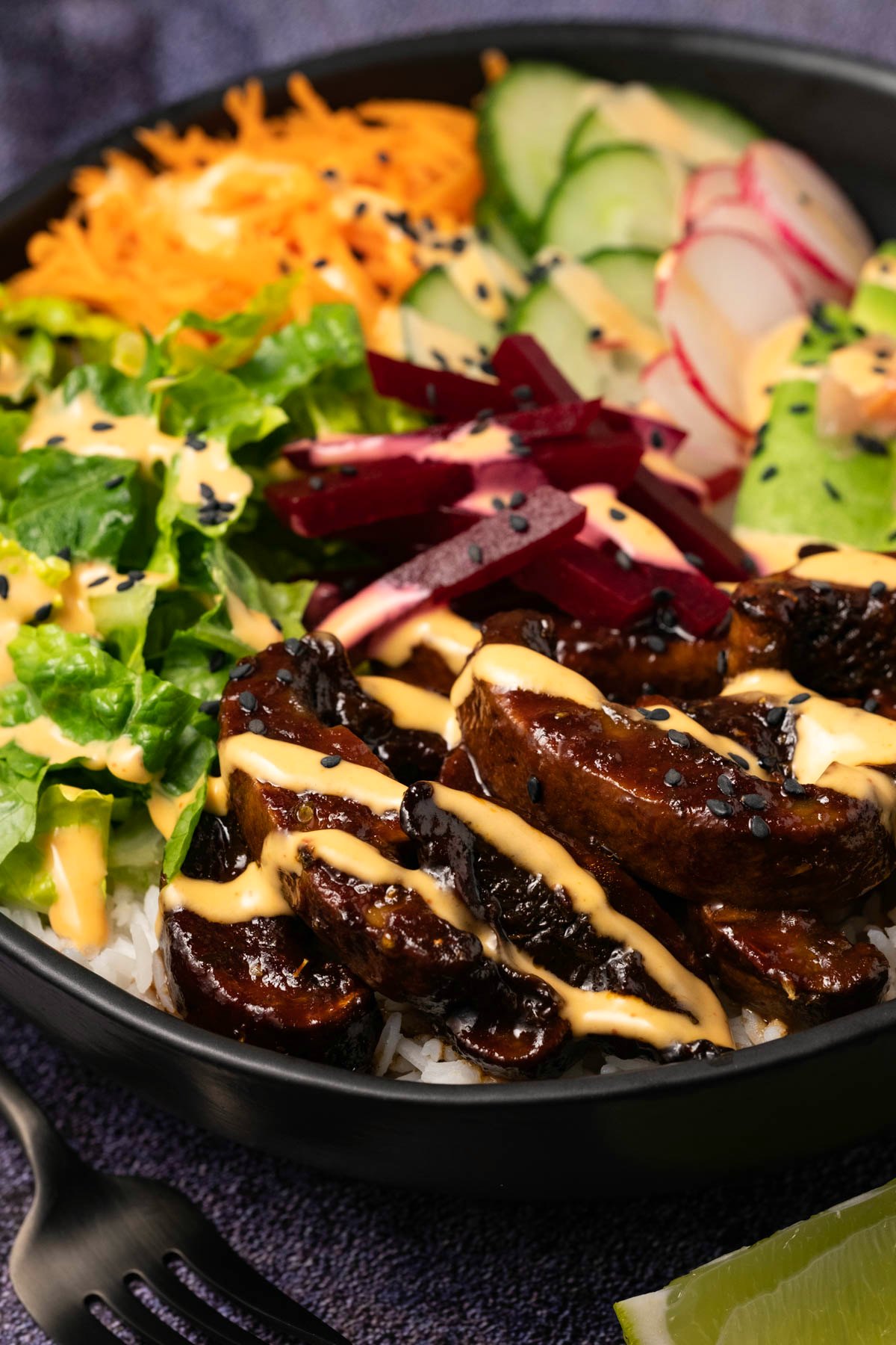 Black bowl filled with mushrooms, salad veggies and rice and drizzled with a creamy dressing. 