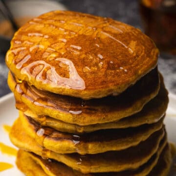 Stack of vegan pumpkin pancakes drizzled with syrup on a white plate.