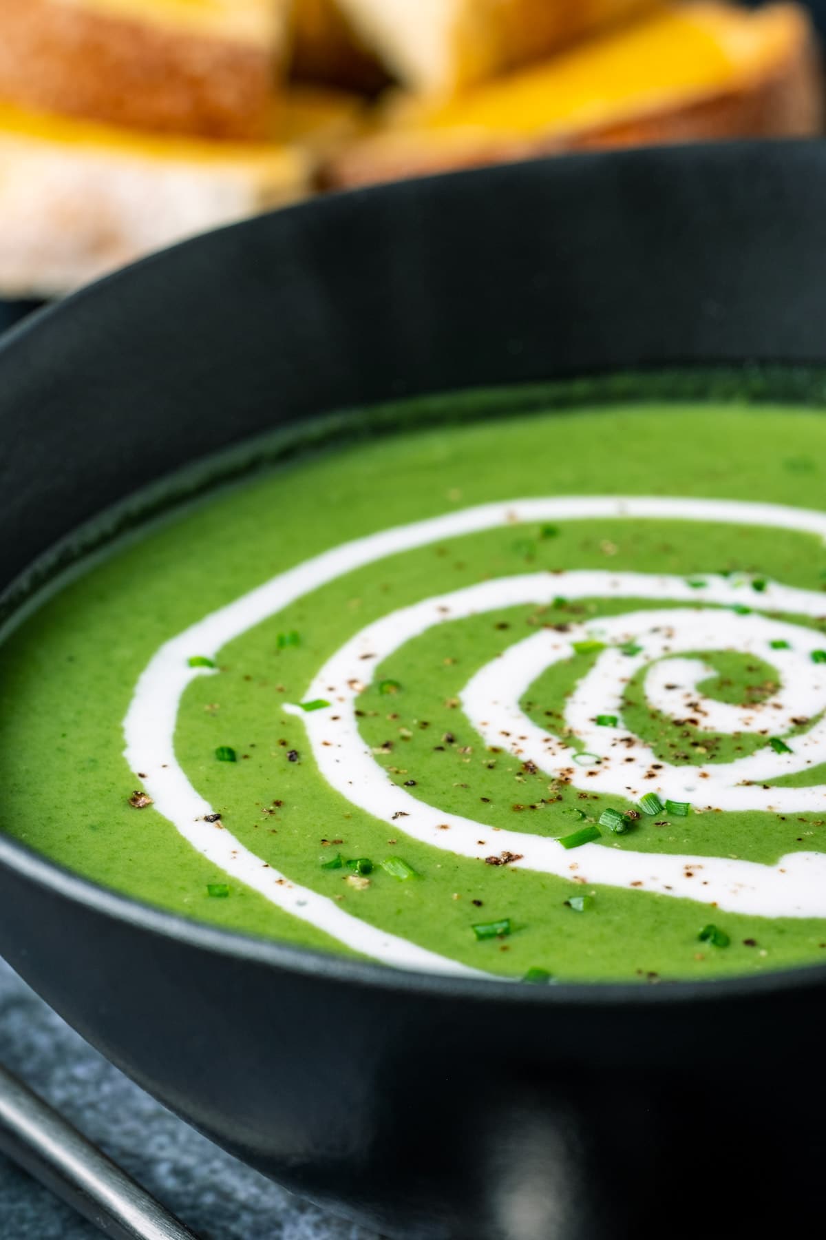 Vegan spinach soup in a black bowl with a swirl of coconut cream on top.