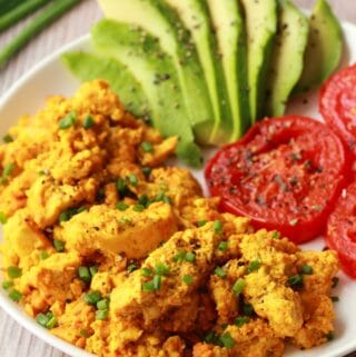 Vegan tofu scramble with sliced avocado and fried tomatoes on a white plate.