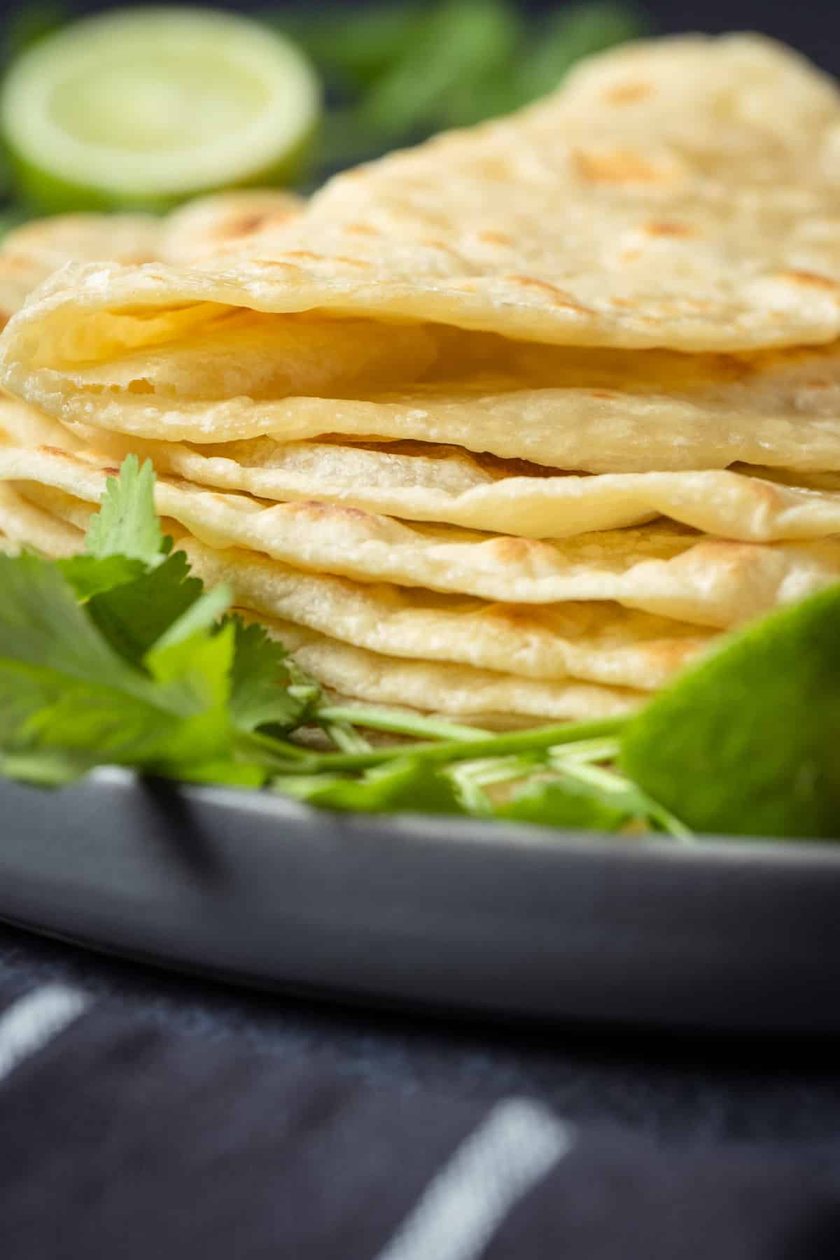 Stack of vegan tortillas on a plate with fresh cilantro.
