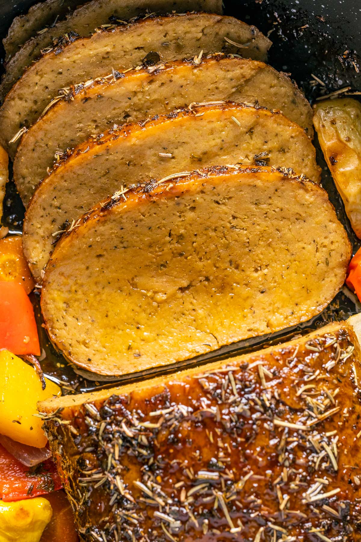 Sliced vegan turkey roast in a roasting pan with vegetables.