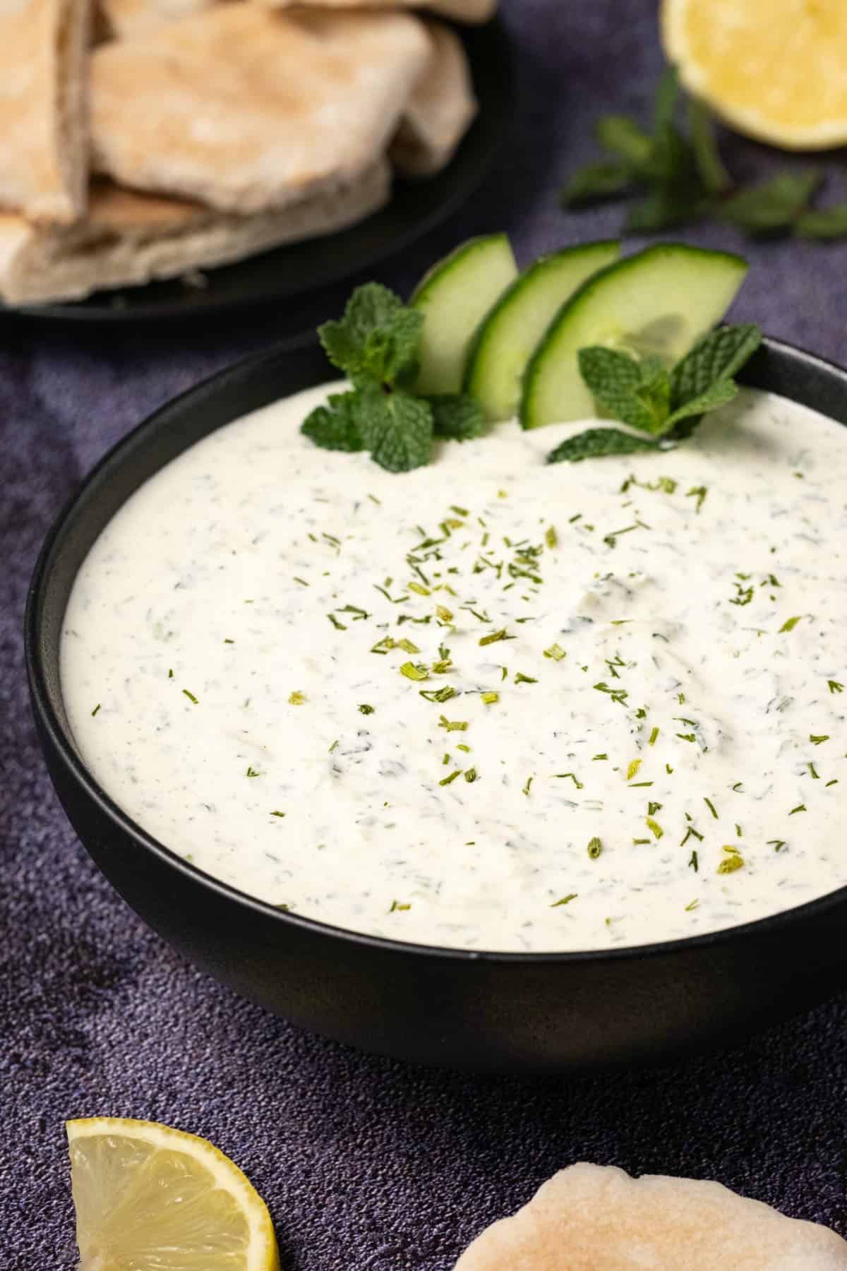 Vegan tzatziki in a black bowl topped with sliced cucumber and fresh mint. 