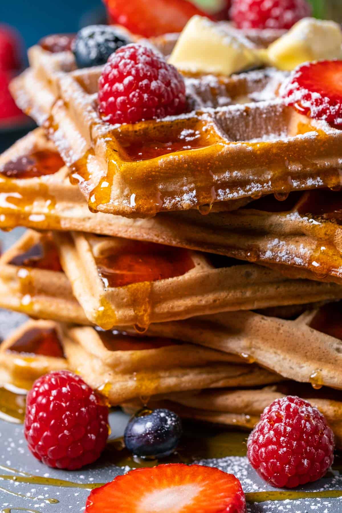 Stack of waffles topped with fresh berries, butter and powdered sugar.