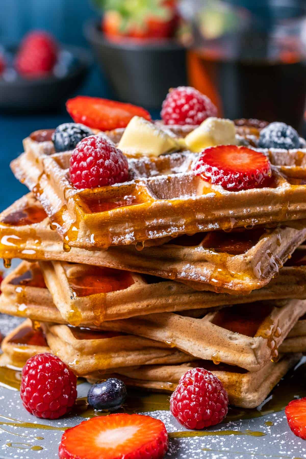 Vegan waffles in a stack topped with vegan butter, powdered sugar and fresh berries.