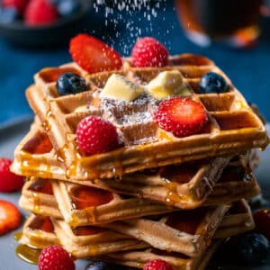 Powdered sugar sprinkling down over a stack of waffles.