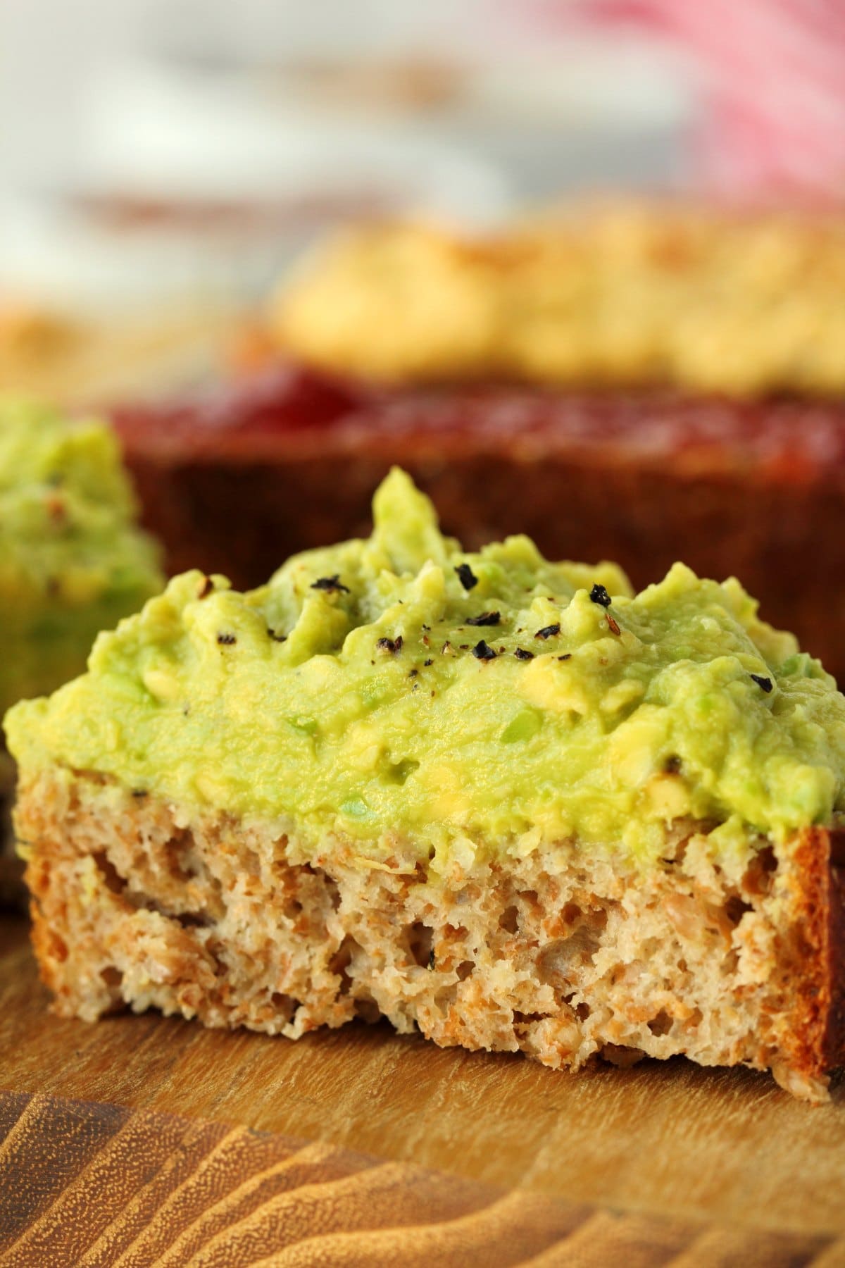 A slice of whole wheat bread topped with avocado and sliced in half. 